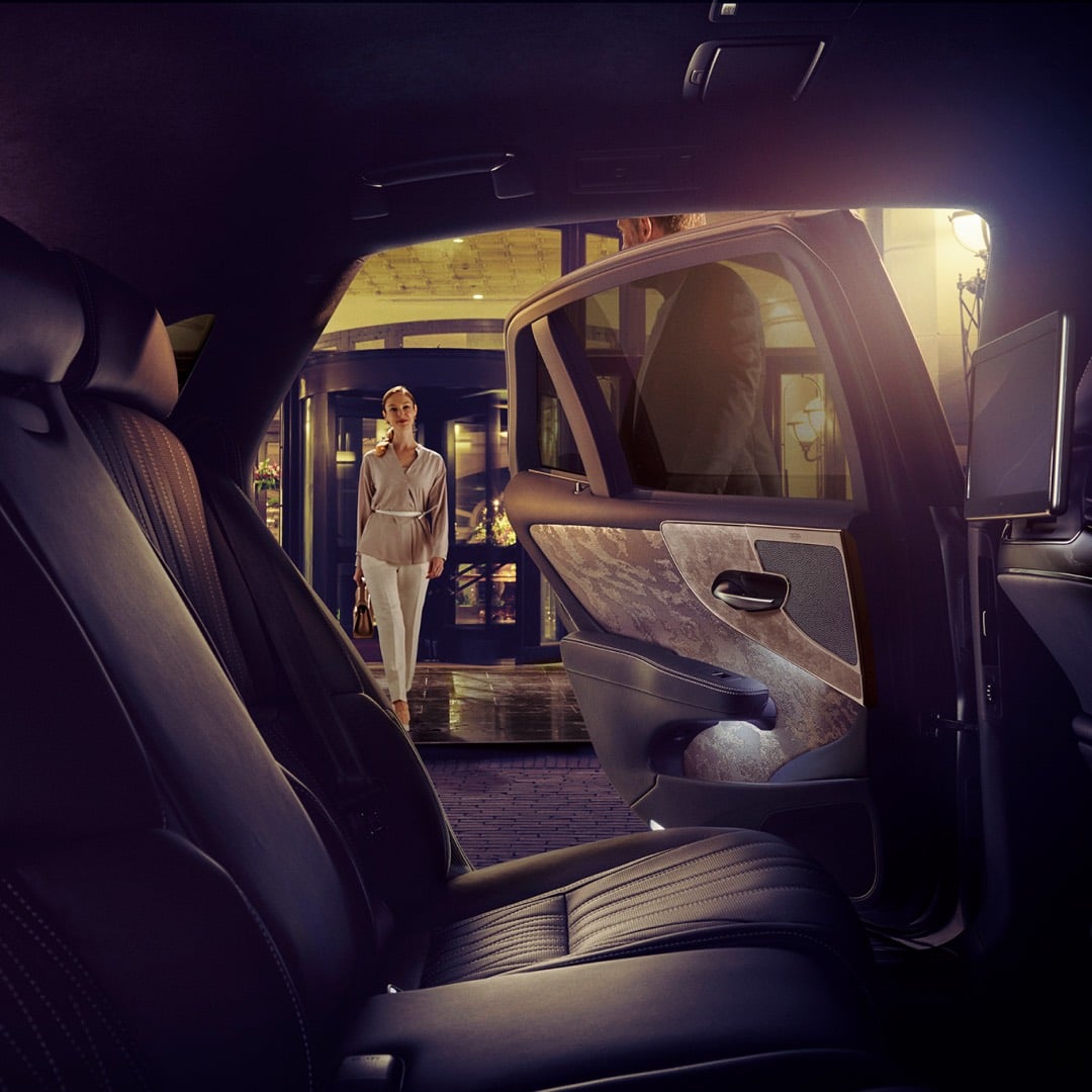 Interior rear view of a Lexus LS with woman approaching the vehicle, rear door held open by a man outside a hotel.